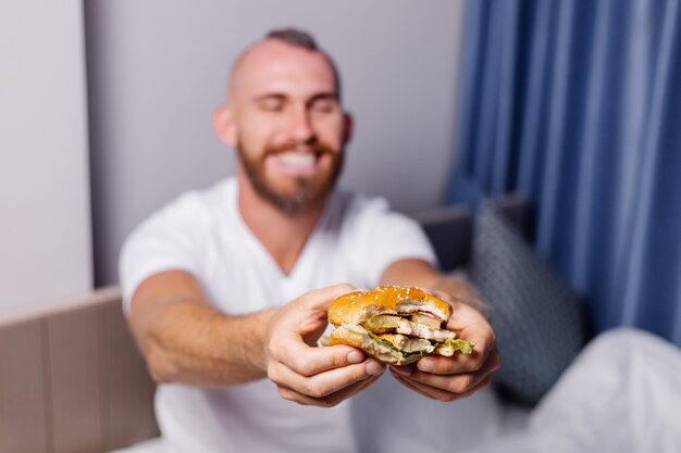 Feliz joven con comida rápida en casa en el dormitorio en la cama