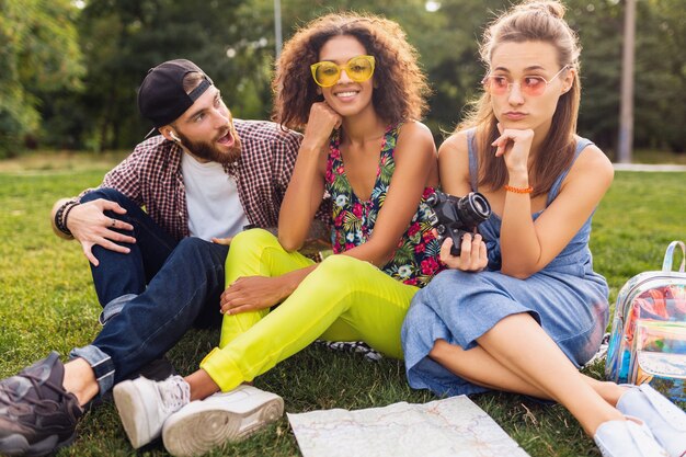 Feliz joven compañía de amigos sentados en el parque viajando mirando en el mapa de turismo, hombres y mujeres divirtiéndose juntos