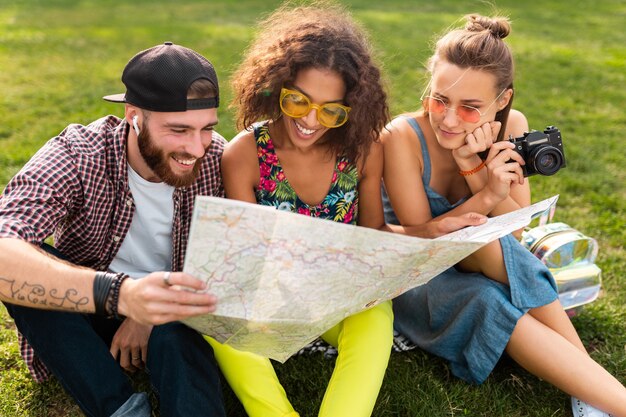 Feliz joven compañía de amigos sentados en el parque viajando mirando en el mapa de turismo, hombres y mujeres divirtiéndose juntos