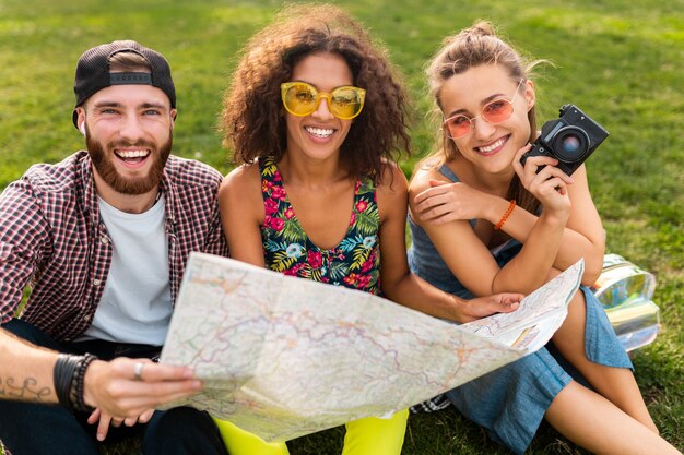 Feliz joven compañía de amigos sentados en el parque viajando mirando en el mapa de turismo, hombres y mujeres divirtiéndose juntos