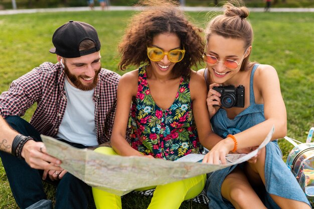 Feliz joven compañía de amigos sentados en el parque viajando mirando en el mapa de turismo, hombres y mujeres divirtiéndose juntos