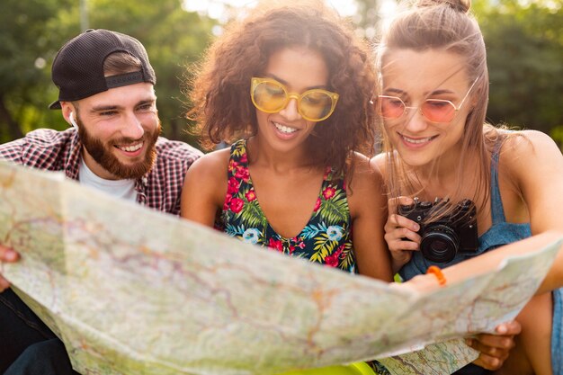 Feliz joven compañía de amigos sentados en el parque viajando mirando en el mapa de turismo, hombres y mujeres divirtiéndose juntos