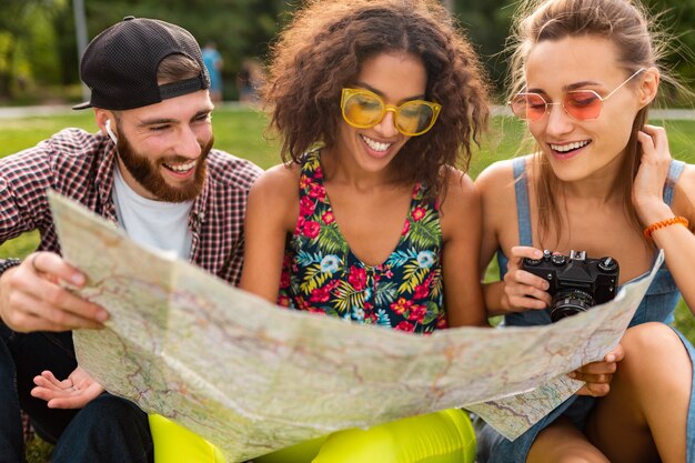 Feliz joven compañía de amigos sentados en el parque viajando mirando en el mapa de turismo, hombres y mujeres divirtiéndose juntos
