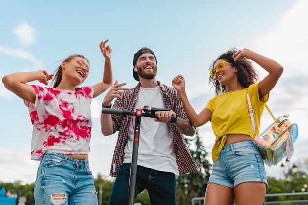 Feliz joven compañía de amigos sonrientes bailando caminando en la calle con patinete eléctrico, hombre y mujer divirtiéndose juntos