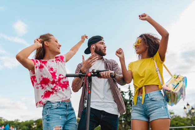 Feliz joven compañía de amigos sonrientes bailando caminando en la calle con patinete eléctrico, hombre y mujer divirtiéndose juntos