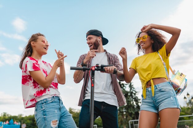 Feliz joven compañía de amigos sonrientes bailando caminando en la calle con patinete eléctrico, hombre y mujer divirtiéndose juntos