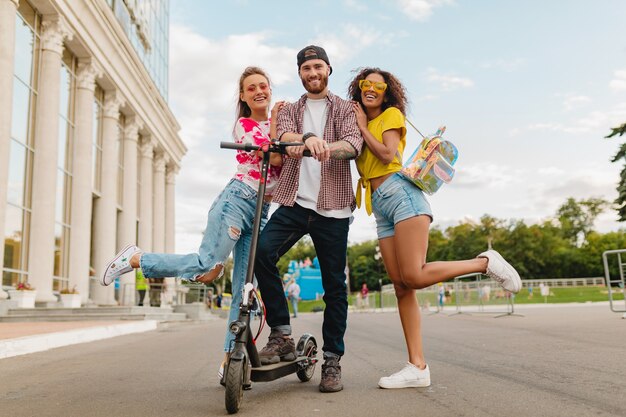 Feliz joven compañía de amigos sonrientes caminando en la calle con patinete eléctrico, hombre y mujer divirtiéndose juntos