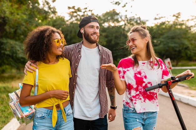 Feliz joven compañía de amigos sonrientes caminando en el parque con patinete eléctrico, hombre y mujer divirtiéndose juntos