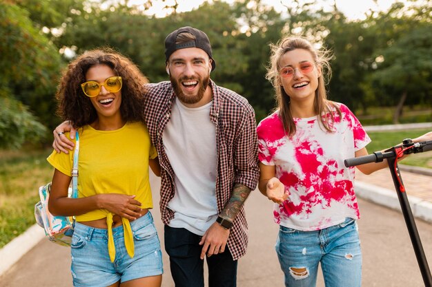 Feliz joven compañía de amigos sonrientes caminando en el parque con patinete eléctrico, hombre y mujer divirtiéndose juntos