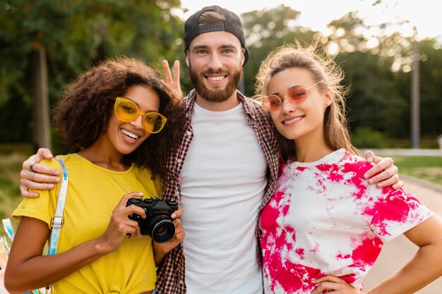 Feliz joven compañía de amigos sonrientes emocionales caminando en el parque con cámara de fotos, hombres y mujeres divirtiéndose juntos