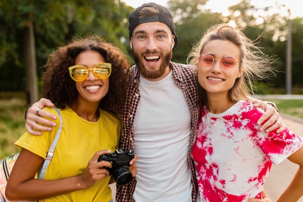 Feliz joven compañía de amigos sonrientes emocionales caminando en el parque con cámara de fotos, hombres y mujeres divirtiéndose juntos