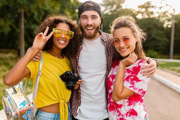 Feliz joven compañía de amigos sonrientes emocionales caminando en el parque con cámara de fotos, hombres y mujeres divirtiéndose juntos