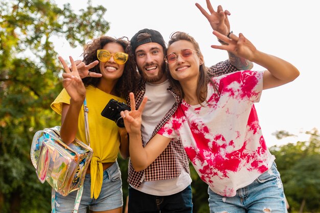 Feliz joven compañía de amigos sonrientes emocionales caminando en el parque con cámara de fotos, hombres y mujeres divirtiéndose juntos