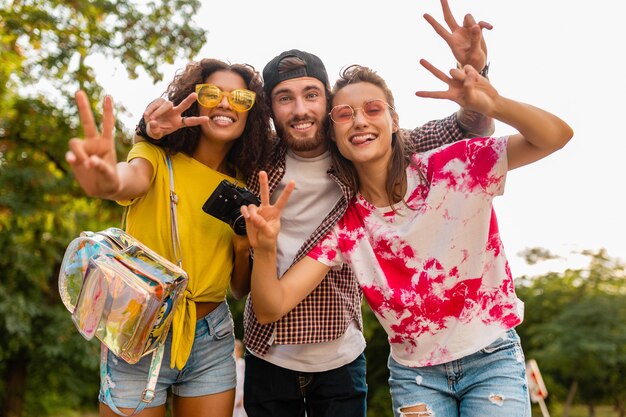 Feliz joven compañía de amigos sonrientes emocionales caminando en el parque con cámara de fotos, hombres y mujeres divirtiéndose juntos