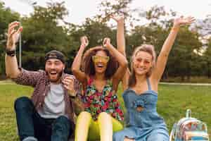 Foto gratuita feliz joven compañía de amigos sonrientes sentado en el parque sobre el césped, hombre y mujer divirtiéndose juntos