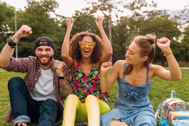 Feliz joven compañía de amigos sonrientes sentado en el parque sobre el césped, hombre y mujer divirtiéndose juntos