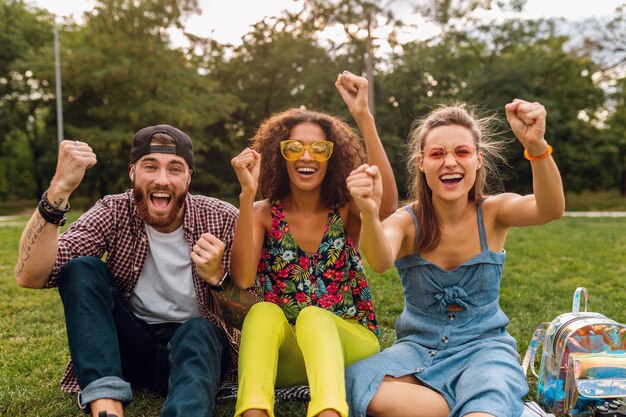 Feliz joven compañía de amigos sonrientes sentado en el parque sobre el césped, hombre y mujer divirtiéndose juntos