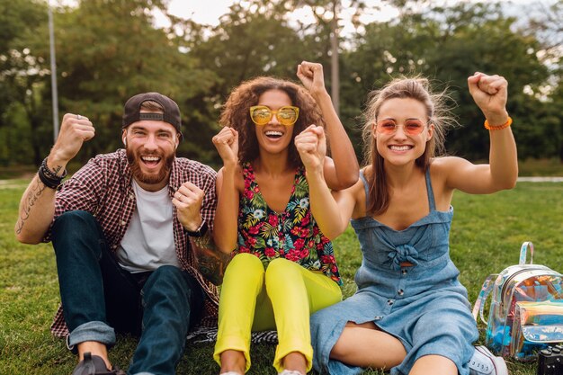 Feliz joven compañía de amigos sonrientes sentado en el parque sobre el césped, hombre y mujer divirtiéndose juntos