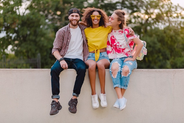 Feliz joven compañía de amigos sonrientes sentados en el parque, hombres y mujeres divirtiéndose juntos