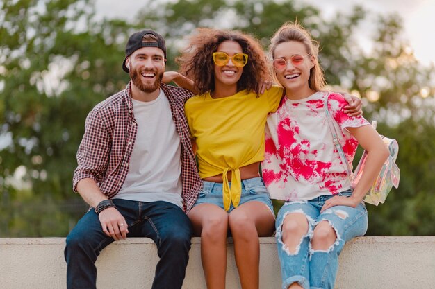 Feliz joven compañía de amigos sonrientes sentados en el parque, hombres y mujeres divirtiéndose juntos