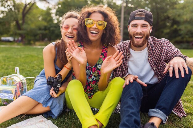 Feliz joven compañía de hablar sonriendo amigos sentados en el parque, hombre y mujer divirtiéndose juntos, viajando con cámara