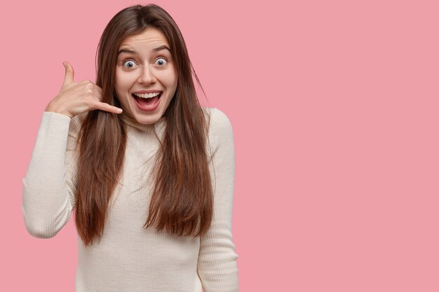 Feliz joven demuestra gesto de llamarme, mantiene la mano cerca de la oreja, mira feliz