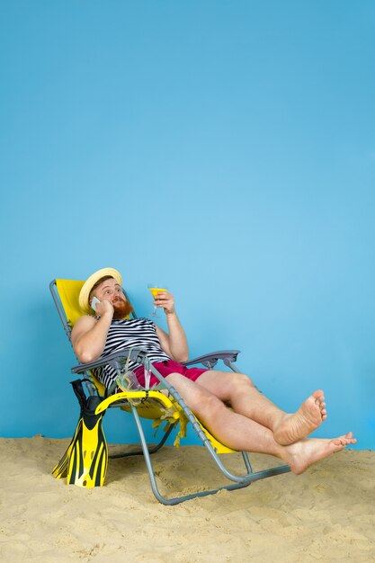 Feliz joven descansando, toma selfie, bebiendo cócteles sobre fondo azul de estudio. Concepto de emociones humanas, expresión facial, vacaciones de verano o fin de semana. Frío, verano, mar, océano, alcohol.