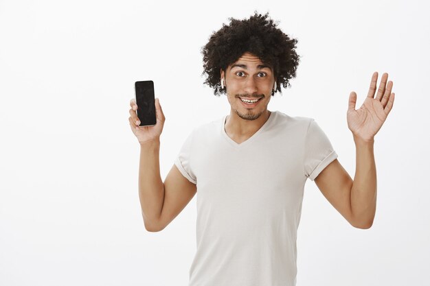 Feliz joven despreocupado sosteniendo teléfono inteligente y escuchando música en auriculares inalámbricos