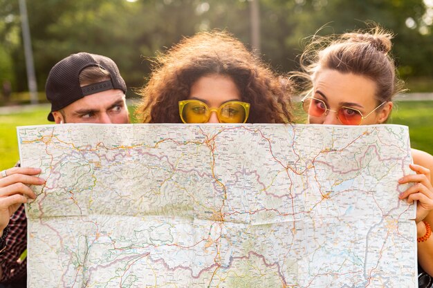 Feliz joven divertida compañía de amigos turistas escondidos detrás del mapa con gafas de sol, hombres y mujeres divirtiéndose juntos, viajando