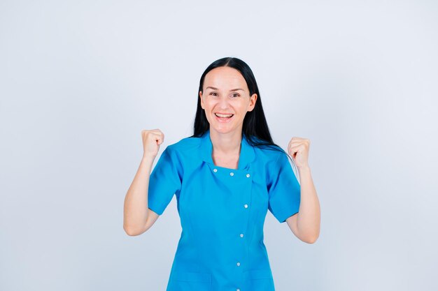 Feliz joven doctor está posando para la cámara levantando los puños sobre fondo blanco.