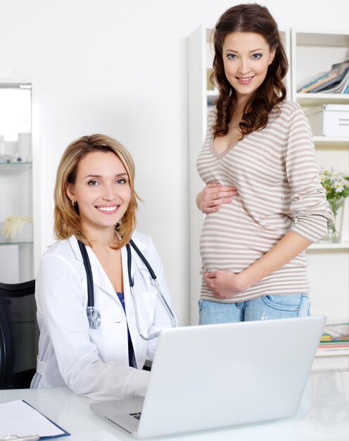 Feliz joven embarazada y su médico con portátil