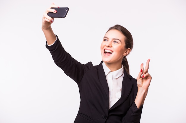 Feliz joven empresaria haciendo foto selfie en smartphone sobre pared blanca