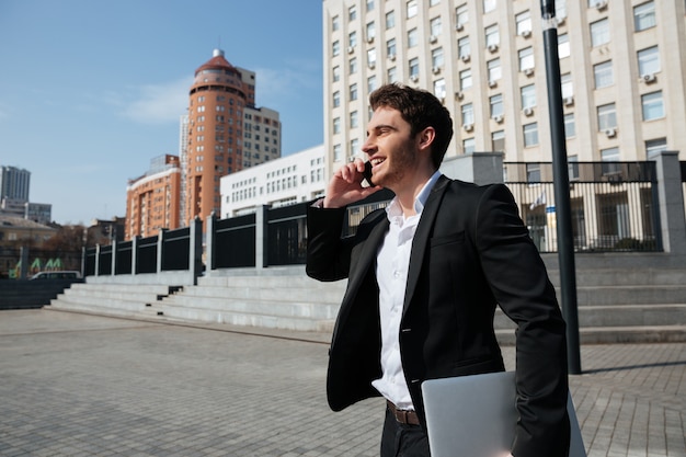 Feliz joven empresario caminando al aire libre hablando por teléfono.