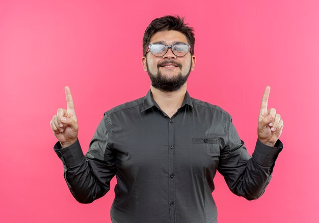 Feliz joven empresario con gafas apunta hacia arriba aislado en rosa con espacio de copia