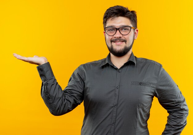 Foto gratuita feliz joven empresario con gafas fingiendo sostener algo aislado en la pared amarilla