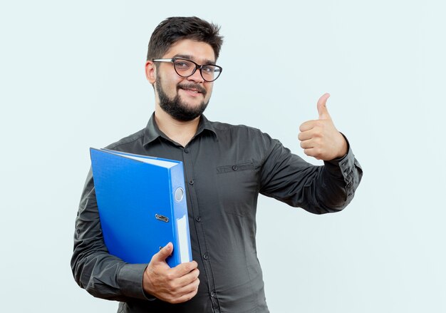 Feliz joven empresario con gafas sosteniendo la carpeta con el pulgar hacia arriba aislado sobre fondo blanco.