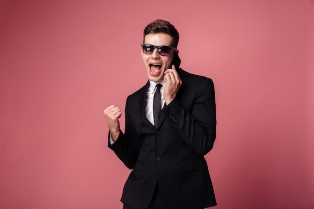 Feliz joven empresario hablando por teléfono hacer gesto ganador.