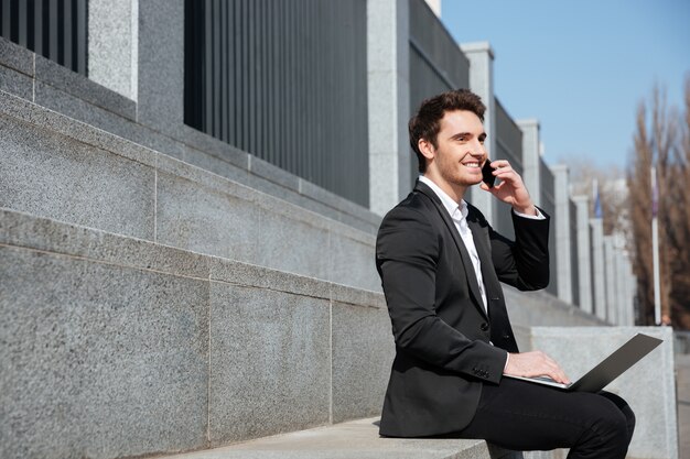 Feliz joven empresario sentado al aire libre hablando por teléfono.