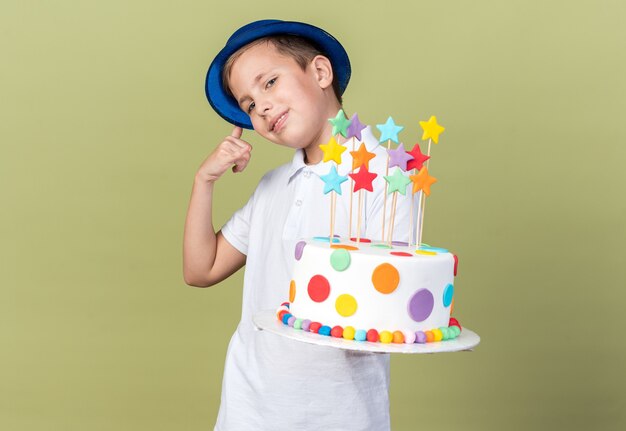 Feliz joven eslavo con gorro de fiesta azul sosteniendo pastel de cumpleaños y gesticulando llámame signo aislado en la pared verde oliva con espacio de copia