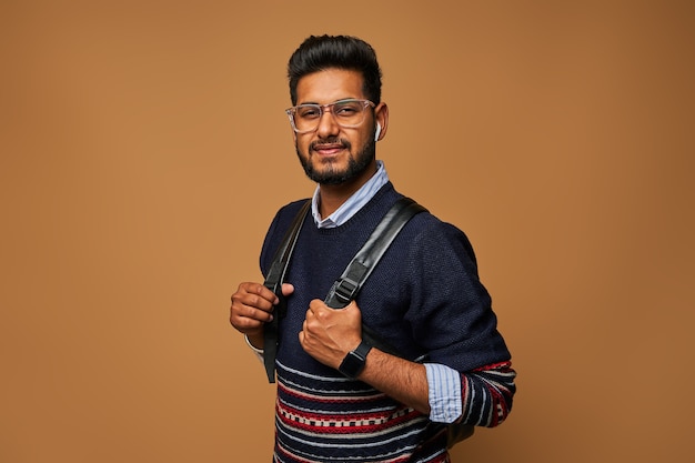 Feliz joven estudiante indio con mochila y gafas en cierre con estilo casual en la pared.