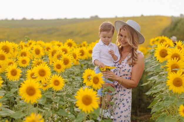 Feliz joven familia, madre, padre e hijo, sonríe, abraza y abraza en el campo de girasol