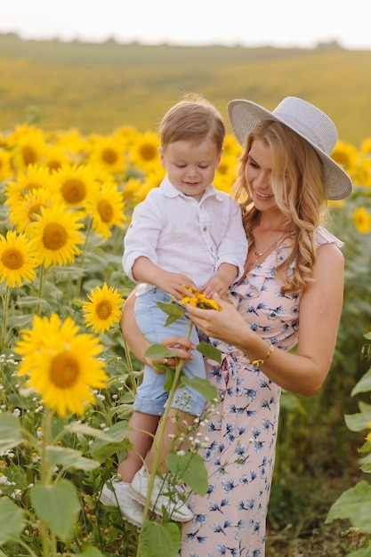 Feliz joven familia, madre, padre e hijo, sonríe, abraza y abraza en el campo de girasol