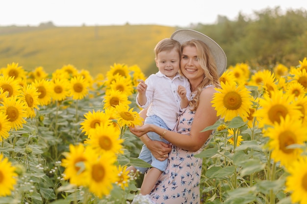 Feliz joven familia, madre, padre e hijo, sonríe, abraza y abraza en el campo de girasol