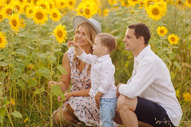 Feliz joven familia, madre, padre e hijo, sonríe, abraza y abraza en el campo de girasol