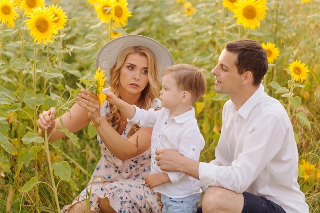 Feliz joven familia, madre, padre e hijo, sonríe, abraza y abraza en el campo de girasol