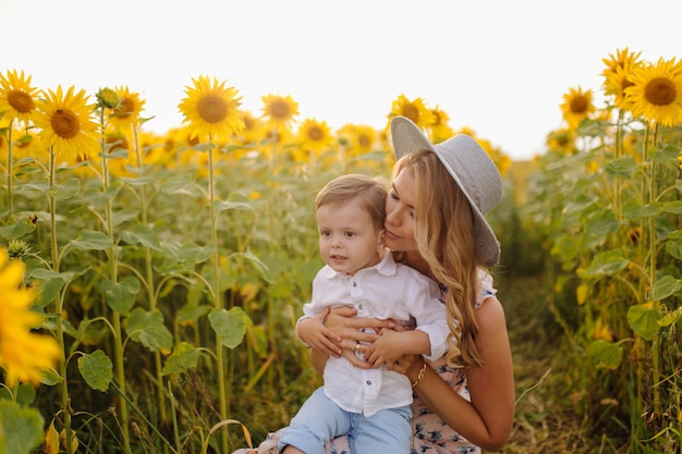 Feliz joven familia, madre, padre e hijo, sonríe, abraza y abraza en el campo de girasol