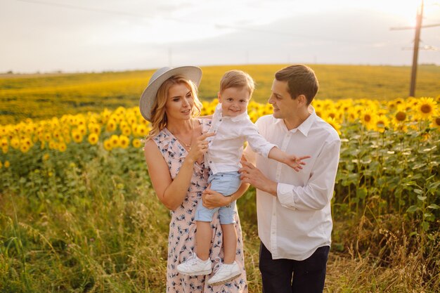 Feliz joven familia, madre, padre e hijo, sonríe, abraza y abraza en el campo de girasol