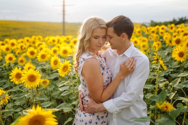 Feliz joven familia, madre, padre e hijo, sonríe, abraza y abraza en el campo de girasol