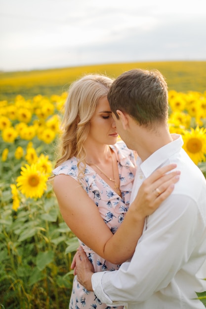 Feliz joven familia, madre, padre e hijo, sonríe, abraza y abraza en el campo de girasol