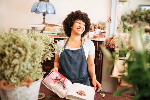 Feliz joven florista femenina con álbum de fotos de flores en la tienda